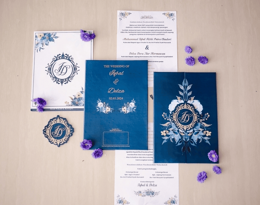 Navy blue and gold monogram wedding invitation suite with floral details laid out on a light background.