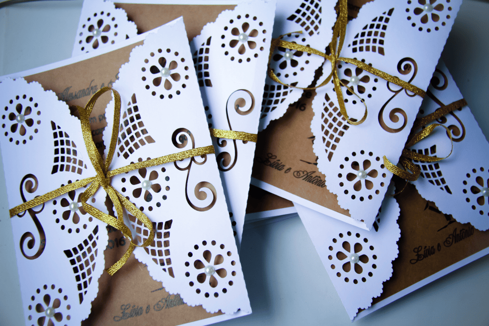 Rustic wedding invitation cards featuring white laser-cut paper lace, kraft paper, and a gold ribbon.