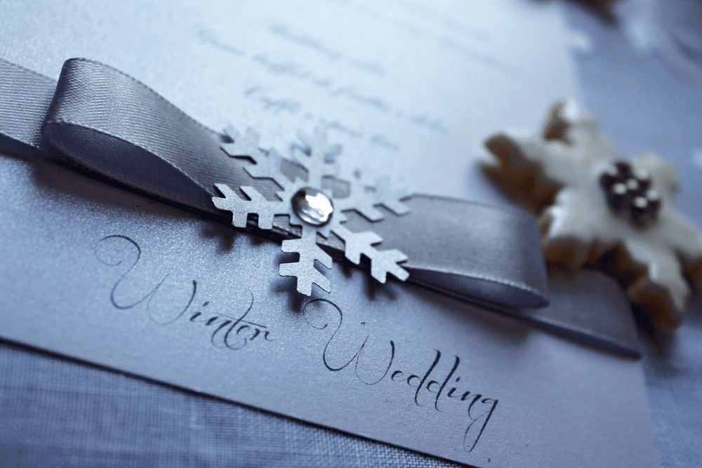 • A silver winter wedding invitation with a grey ribbon and a snowflake embellishment.