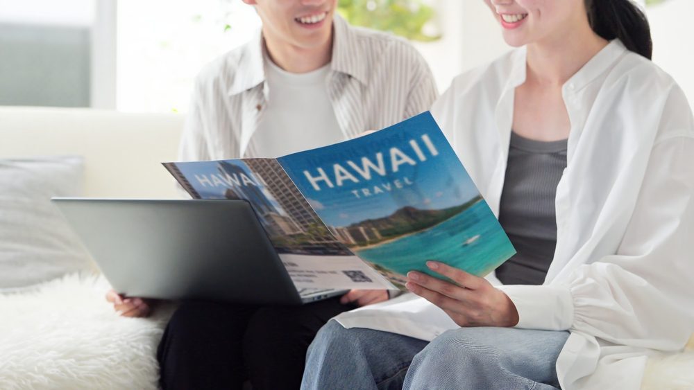 wo people sitting together looking at a "Hawaii Travel" leaflet and a laptop, illustrating a guide about double-sided printing and paper opacity.