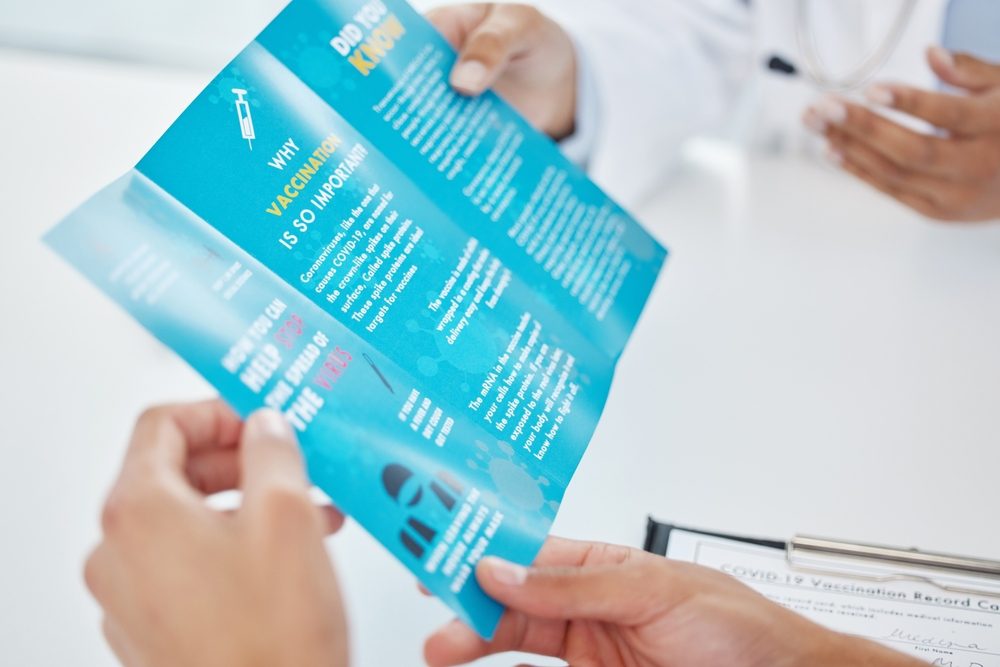A screenshot of an article titled "Leaflet, Flyer, or Brochure? What's the Difference?" featuring a photo of hands holding a blue tri-fold vaccination brochure. 